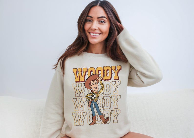 a woman sitting on a couch wearing a woody sweatshirt