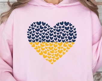 May include: A pink hoodie featuring a heart-shaped design made up of blue and yellow hearts. The heart symbolises the Ukrainian flag.