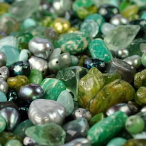 May include: A collection of green, blue, and gray gemstones and pearls. The stones are various shapes and sizes, and some have a shiny, iridescent finish.