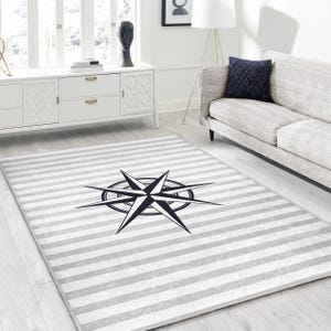 May include: A gray and white striped rug with a black compass design in the center. The rug is on a light wood floor.