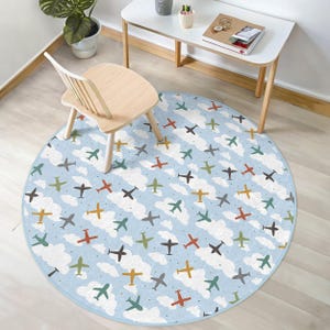 May include: A blue and white round rug with a repeating pattern of airplanes on a cloud background. The rug is on a light wood floor and a wooden chair is in the background.