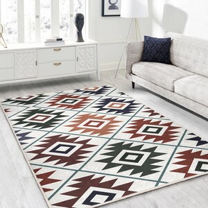 Puede incluir: Una alfombra blanca con un patrón geométrico en tonos marrones, rojos, verdes y azules. El patrón presenta una serie de cuadrados y triángulos.
