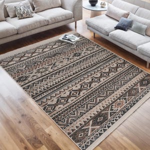 May include: A beige and brown area rug with a geometric pattern. The rug has a fringe border and is made of a woven material.