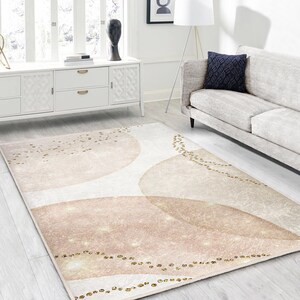 Peut inclure: Un tapis de salon rose poudré et crème avec un léger scintillement et un motif géométrique de cercles qui se chevauchent et de paillettes dorées éparpillées.