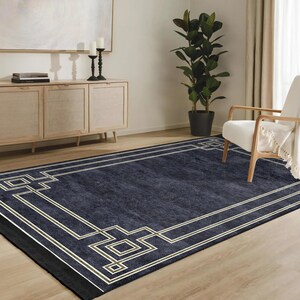 May include: A navy blue area rug with a geometric pattern in a cream and gold color. The rug has a black border and is shown in a living room setting.