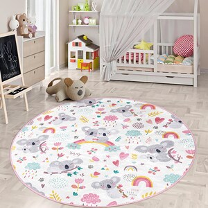 Könnte beinhalten: Ein runder weißer und rosa Teppich mit einem bunten Regenbogenmuster und niedlichen Koalabären. Der Teppich hat ein sich wiederholendes Muster aus Koalas, Regenbögen, Herzen und Sternen.