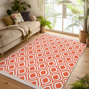 Puede incluir: Una alfombra geométrica con estampado blanco y naranja con un borde blanco. La alfombra tiene un patrón repetitivo de líneas curvas y círculos.