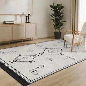 May include: A black and white geometric patterned rug with a cream background. The rug has a fringe border and is laid out on a wooden floor.