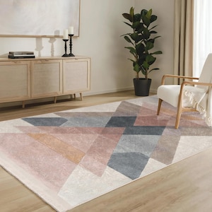 Peut inclure: Un tapis à motifs géométriques dans des tons de rose, gris et beige. Le tapis est posé sur un sol en bois dans un salon.