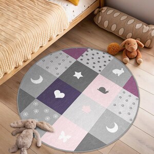 May include: A round, multi-colored play mat with a patchwork design. The mat features various shapes, including stars, hearts, moons, and a snail. The mat is perfect for a child's playroom or nursery.
