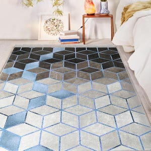 Pode incluir: Um tapete com padrão geométrico em um esquema de cores azul claro e cinza. O tapete apresenta um padrão repetitivo de cubos 3D.