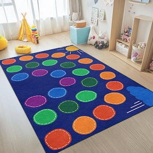 Puede incluir: Una alfombra de juego azul con círculos punteados de colores en naranja, verde, morado y azul. La alfombra presenta un diseño de sol y nube, perfecto para una sala de juegos o un dormitorio infantil. La alfombra está diseñada para niños.