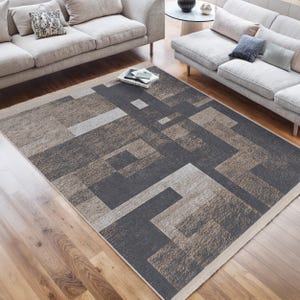 May include: A geometric patterned rug with a dark grey and beige colour scheme. The rug is laid out on a hardwood floor in a living room setting.