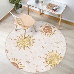 Pode incluir: Um tapete redondo de cor creme com um padrão repetitivo de sóis estilizados em tons de laranja, amarelo e castanho. O tapete é decorado com pequenas estrelas brancas e arco-íris.