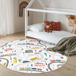 May include: A round, white play rug with a colorful road and train track design. The rug features cars, buses, trains, and trees.