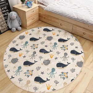 Peut inclure: Un tapis de jeu rond de couleur crème avec un thème nautique. Le tapis présente un motif répétitif de baleines, d'étoiles de mer, de coquillages et de coraux. Le tapis est parfait pour la salle de jeux ou la chambre d'un enfant.