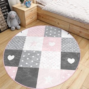 Könnte beinhalten: Eine runde rosa und graue Spielmatte mit Patchwork-Design mit Herzen, Sternen und Punkten.