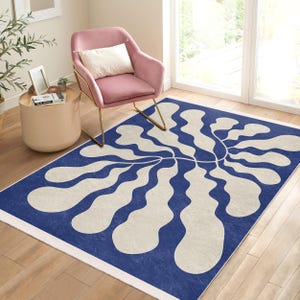 May include: A blue and white abstract area rug with a large, stylized floral design. The rug has a white border and is laid out on a hardwood floor.