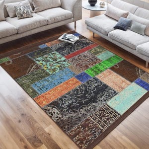 Può includere: Un tappeto patchwork colorato con un bordo marrone. Il tappeto è composto da quadrati e rettangoli di diversi colori, tra cui verde, blu, rosso, arancione e marrone. Il tappeto è steso su un pavimento in legno.