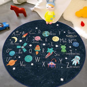 May include: A round, blue play mat with a space theme. The mat features the alphabet, planets, stars, rockets, and other space-related imagery. The letters are in white and the words are in black. The mat is perfect for a child's playroom or bedroom.