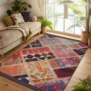 Op de afbeelding: Een kleurrijk patchwork tapijt met een geometrisch ontwerp. Het tapijt is gemaakt van verschillende stoffen en kleuren, waaronder rood, blauw, groen, geel en bruin. Het tapijt ligt op een houten vloer in een woonkamer.