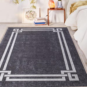 May include: A dark gray area rug with a white geometric border. The rug has a distressed, vintage look.