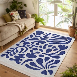 Puede incluir: Una alfombra blanca con un patrón floral azul. La alfombra tiene un diseño moderno y abstracto con formas grandes y orgánicas.