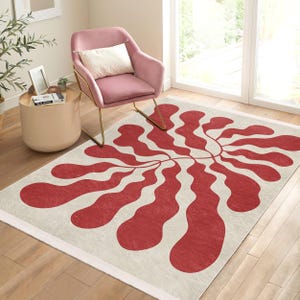 Könnte beinhalten: Ein abstrakter roter und weißer Teppich mit einem wellenförmigen, organischen Design. Der Teppich hat einen weißen Rand und liegt auf einem Holzboden.