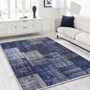 Pode incluir: Um tapete de patchwork azul e branco com um visual desgastado. O tapete tem uma variedade de quadrados e retângulos de diferentes tamanhos em tons de azul e branco. O tapete está colocado sobre um piso branco em uma sala de estar.