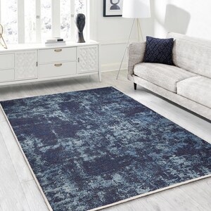May include: A blue and gray abstract patterned area rug with a white border. The rug is laid out on a white floor in a living room setting.