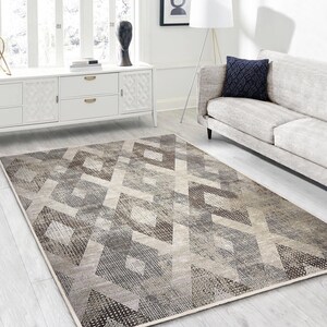 May include: A grey and brown geometric patterned area rug with a diamond design. The rug is on a light beige floor in a living room setting.