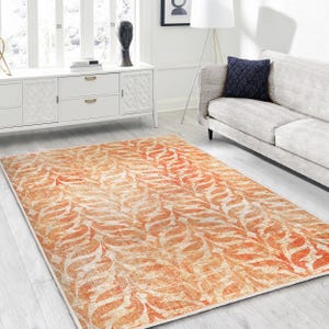 Puede incluir: Una alfombra grande con un patrón de hojas naranja y blanco. La alfombra tiene un aspecto desgastado y vintage.