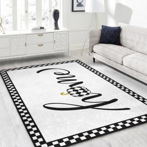 Peut inclure: Tapis à carreaux noirs et blancs avec le mot "famille" écrit en cursive noire. Une citrouille à carreaux noirs et blancs avec une tige dorée se trouve au centre du tapis.