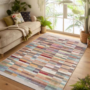 Könnte beinhalten: Ein bunter rechteckiger Teppich mit einem geometrischen Muster aus mehrfarbigen Streifen. Der Teppich hat einen hellbeigen Hintergrund mit einem dezenten Glanz.