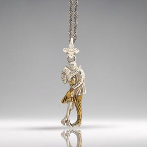 May include: Silver-toned pendant necklace featuring a couple embracing. The pendant has a detailed design with gold and silver accents, depicting a man and woman in an intimate pose. The necklace has a delicate chain and a decorative clasp.