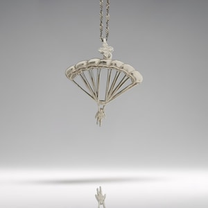 May include: A silver pendant necklace with a parachute design. The parachute is open, with a small figure suspended beneath. The chain is a twisted rope style. The pendant is likely made of sterling silver. The necklace is a stylish accessory.