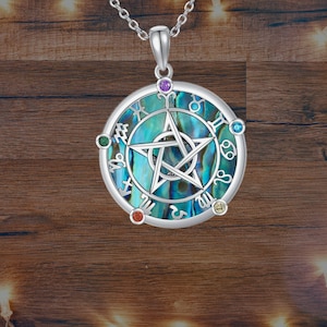 Puede incluir: Un collar con un colgante de plata redondo de nácar azul y verde. El colgante presenta un pentagrama plateado con un círculo alrededor y símbolos del zodíaco alrededor del borde exterior. El colgante tiene cinco pequeñas piedras preciosas de colores alrededor del borde.