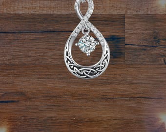 Puede incluir: Un collar con colgante plateado con un diseño de símbolo de infinito. El colgante presenta una forma de lágrima con nudos celtas y una piedra preciosa central brillante. El collar se muestra sobre una superficie de madera.