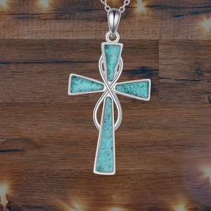 May include: Silver pendant necklace with a turquoise cross design. The cross is a simple, elegant design with a knot in the center.