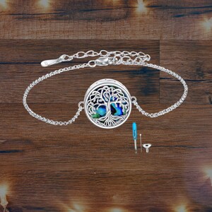 May include: Silver bracelet with a circular pendant depicting a tree of life. The pendant has a blue and green iridescent background. Includes a small blue tool and funnel.