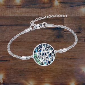 May include: Silver-toned bracelet featuring a circular pendant with a star design and text. The pendant has a blue, green, and white color scheme. The bracelet is on a wooden surface.