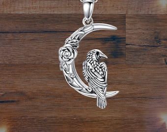 May include: Silver pendant necklace featuring a crescent moon with a detailed raven perched on a branch, surrounded by floral accents.
