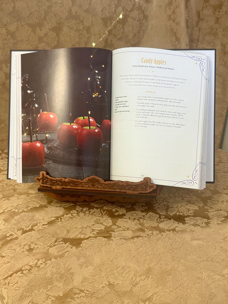 Puede incluir: Un libro de cocina abierto en una p&aacute;gina titulada "Candy Apples" con una receta para hacer manzanas de caramelo. La p&aacute;gina presenta una foto de manzanas de caramelo rojas sobre una superficie negra.