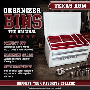 May include: A white metal toolbox with an open lid revealing four rectangular red organizer bins inside. The front of the toolbox features the Kobalt brand name. A metal ratchet and four silver sockets are positioned on the surface in front.