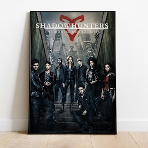 May include: A poster for the TV show "Shadowhunters: The Mortal Instruments" featuring the main cast standing on a set of stairs. The poster has a black background with a red rune symbol in the top center.