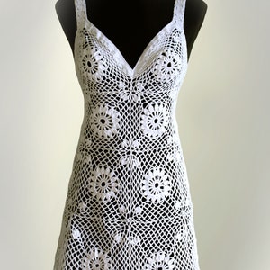 Puede incluir: Vestido blanco de crochet con cuello en V y un patrón floral. El vestido es sin mangas y tiene un ajuste holgado.