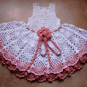 Puede incluir: Vestido blanco de crochet con un ribete degradado rosa y un adorno de flor de crochet rosa en la cintura.