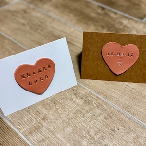 May include: Two handmade cards with heart-shaped decorations. One is white with a heart reading "MR & MRS GOLD". The other is brown with a heart reading "12.05.13". Both hearts are a reddish-orange colour.