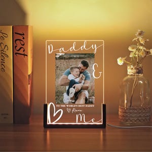 May include: A personalized LED photo frame with the words "Daddy & me" and "To the world's best Daddy". The frame features a photo of a father and child. The base is black, and the light is warm.