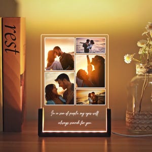 May include: A personalised LED photo display with a wooden base. The acrylic panel features six romantic photos and the quote, "In a sea of people, my eyes will always search for you." The warm light illuminates the images, creating a sentimental gift.